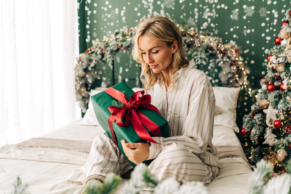Attractive happy woman sitting on bed in christmas time opens gift boxes