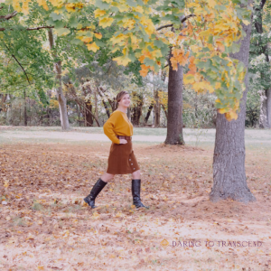 Woman walking in a park between trees. The leaves are gold and the ground is covered with leaves too.